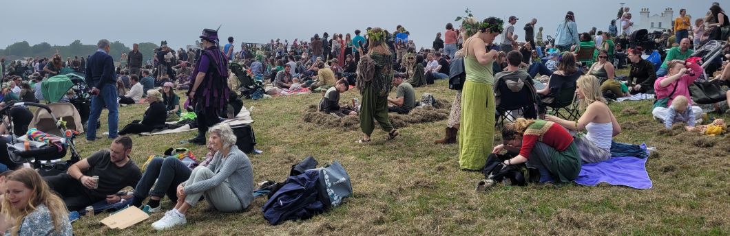 a large number of attendees sitting on Hastings West Hill, some costumed or wearing ivy headdresses